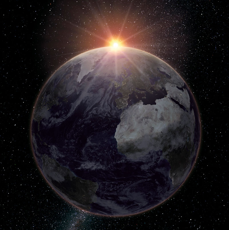 Photograph of Earth from orbit with sunlight breaking over the horizon against the darkness of space